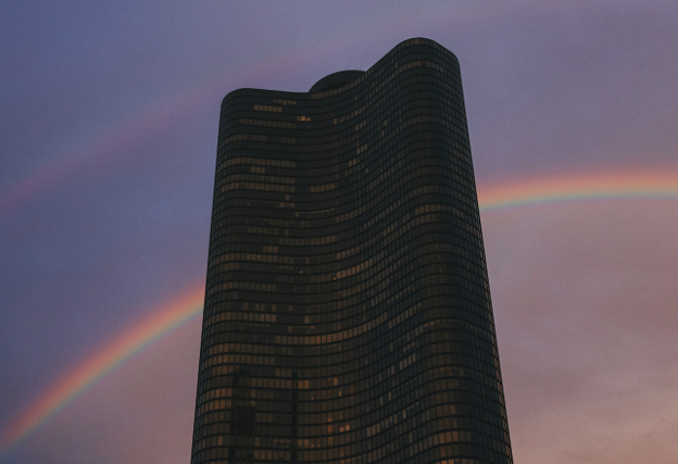 Modern curved glass skyscraper with two rainbow arcs in a dusky sky on sunset.